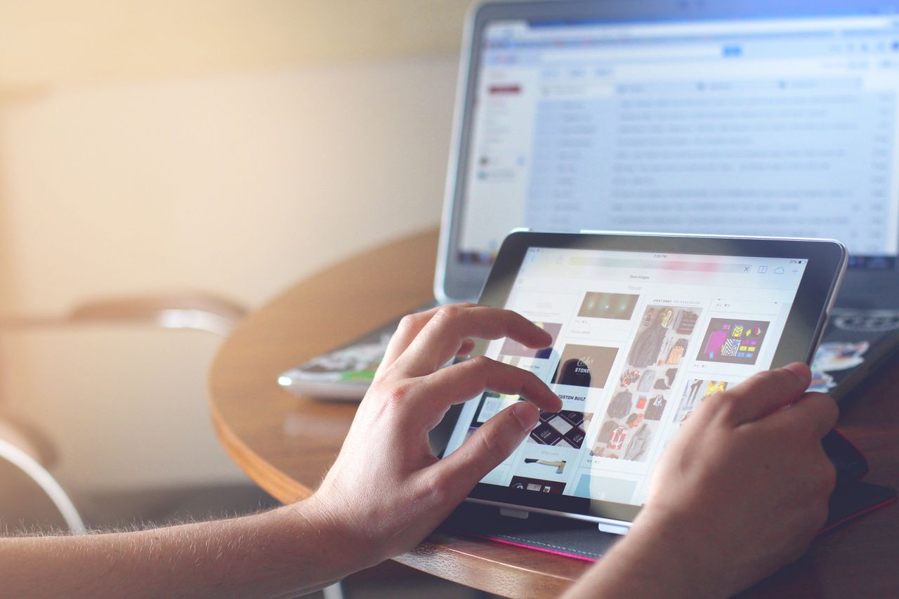 The Art of Drawing Readers In: Your attractive post title goes here Hands using a tablet beside a laptop in a home office setting, showcasing online browsing.