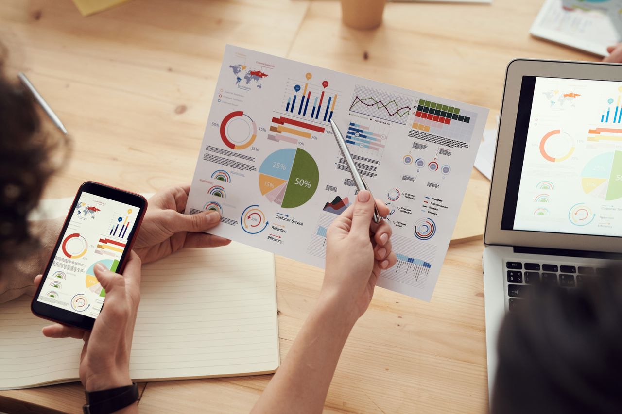 why-choose-us Team members analyze charts during a business meeting with laptops and smartphones.