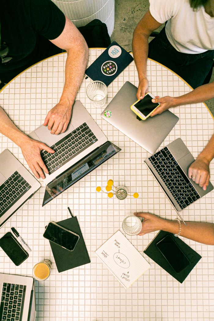gallery-1 Top view of a team collaborating with laptops, phones, and notes in a modern office.